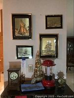 View of the antique mantel clock on table surface with nautical prints framed and hung on the wall behind, including mantel clock key and some decor items on the table.