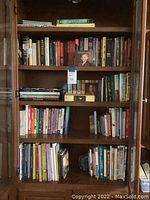 Full view of five wooden shelves filled with books from varied genres including religious texts and biographies.