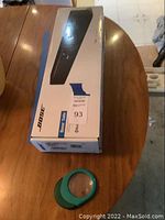 Bose Solo Speaker box standing vertically on a wooden table, showing part of the box and logo.