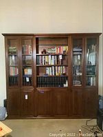 Full front view of the large wooden cabinet and bookshelf unit showing glass panel doors, shelves with books, and lower solid doors.