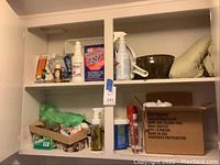 Wide view of white cabinet displaying various cleaning supplies including TSP box, spray bottles, cleaning cloths and miscellaneous cleaning accessories.