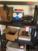 Full view of upper and middle shelves showing First Alert smoke alarm package, vintage lantern, black electronic device possibly a police scanner or radio, alarm clock, and open boxes containing miscellaneous small items.