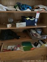 Wooden shelving showing folded fabric items, a blue basket, small glass bottles, and wicker tray with various small items