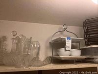 Clear glass decanters, crystal bowl, pitcher, and white dish set with metal stand arranged on shelf.