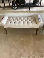 Full front view of cream upholstered lady bench with tufted seat and wooden legs.