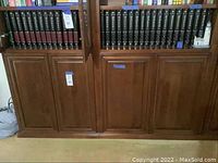 Wide view of all encyclopedia volumes on wooden shelves showing full set with consistent black spines and red labels.