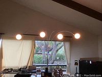 Lamp in living room showing five lit spherical glass lampshades on curved chrome arms extending from central pole.