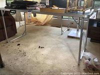 Full view of folding table showing its aluminum legs and metal top with some items placed on it.