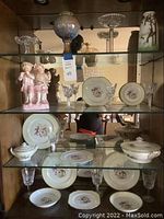 Wide view of shelf with porcelain plates, crystal glasses, figurines, and decorative glass bowl