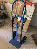Front view of the blue dolly showing solid steel frame and base plate with large tires and rope tied at handle.