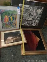 Four framed art pieces arranged on floor: colorful bird print, M.C. Escher black and white print, landscape photo, and sunset/dawn canvas painting