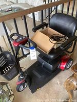 Red three-wheel mobility scooter with black vinyl seat, front basket, and control panel on delta tiller.
