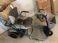 Side view of blue and grey electric mobility scooter with front wire basket, padded seat, armrests and charger cable on seat