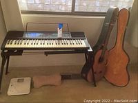Wide shot showing Kawai keyboard on stand and Orlando guitar in case leaning against wall below window
