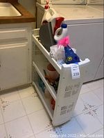 Slender white utility shelf filled with assorted cleaning supplies in laundry or utility room environment.