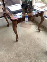 Full side view of the carved wood side table showing the carved legs and wood frame with glass top.