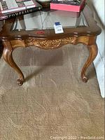 Full view of wooden side table with glass top and decorative carved apron.