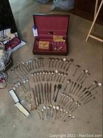 Overview of sterling silver flatware spread on floor with storage chest