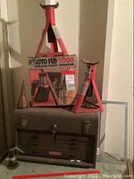 Photo of toolbox with Craftsman branding, Goto Flo 3000 airless paint sprayer box placed atop, and two red jack stands beside it