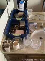 Photo of bathroom counter with blue bins holding jewelry and watches, ceramic cups and crystal glass containers in front.
