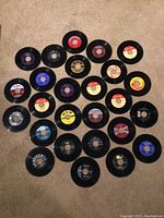 A selection of 25 45 RPM vinyl records laid out with labels visible showing labels such as Capitol, MGM, Columbia, and Decca.
