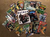 Wide view of comics and book spread on floor showing variety of DC comic books and Batman visual history hardcover book in center.