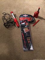 Photo showing the full lot: The Club steering wheel lock in packaging, shop light, booster cables in pouch, and red bottle jack with handle.