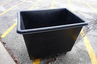 Black plastic cart with large open mouth, shown outdoors on pavement with yellow parking lines. The cart has visible scratches and wear marks.