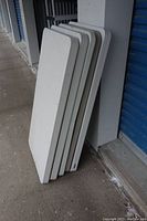 Five white rectangular tabletops stacked vertically and leaning against a wall.