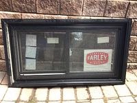 Full front view of black framed sliding window with Farley Windows label visible.