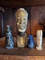 Front view of four stone and mineral figurines and busts on a wooden surface, showing size and material variety