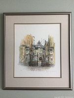 Frontal view of framed architectural watercolor and ink artwork showing iron gate and buildings underneath bare trees.