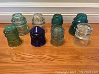 Group of 8 vintage glass electrical insulators in different colors on wood floor