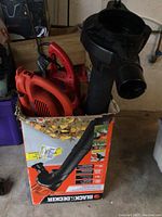 Photo showing the Black+Decker leaf blower nozzle standing in the box along with a red electric hedge trimmer inside the box.