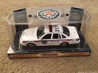 Front side view of the white Metropolitan Police model car in clear plastic display case showing police decals, light bar, and limited edition base.