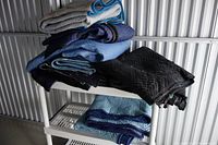 Folded moving blankets in black, navy blue, medium blue, light blue, and gray placed on a white metal rack.