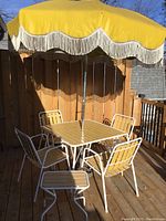 Retro patio set showing square table with six chairs and open yellow umbrella on wooden deck