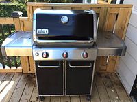 Front view of Weber Genesis three-burner gas grill on wheeled cart with side tables