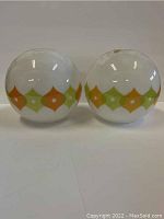 Two round white glass globe light attachments with an orange and green diamond pattern, side by side.
