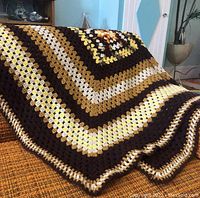 Angled view of the Afghan throw blanket draped over a surface showing color pattern and texture.