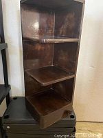 Front angle view of the wooden corner shelf showing three tiers and dark finish, with visible wear on shelves and edges.