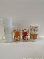 Set of 5 FireKing mugs, 3 white, 1 orange, 1 red, with 2 gold fleck mid-century drinking glasses.