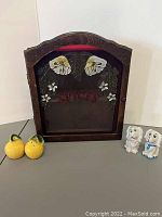 Wooden spice rack with glass door showing floral and leaf motifs and 'SPICES' painted in red, with lemon-shaped and dog-shaped salt and pepper shakers beside it.
