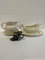 Full view of white ceramic pitcher with saucer and gravy boat with saucer alongside metal bird-shaped salt and pepper shakers