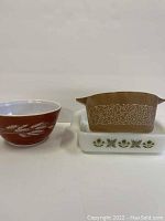 Three Pyrex dishes displayed side by side: reddish-brown Autumn Harvest nesting bowl, brown Woodland casserole dish atop white Fireking dish.