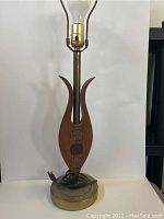 Frontal view of the mid century teak table lamp showing wood centerpiece, metal base with patina, brass socket and clear light bulb.