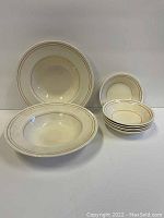 Full view of 2 larger cereal bowls and 6 smaller side bowls stacked, showing decorative thin orange and brown rings on cream ceramic.