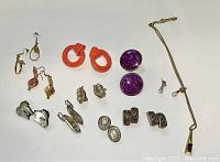Top down photo of assorted vintage earrings and one necklace on a white background showing variety in colors, materials and styles.