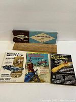 Photo showing three Popular Mechanics magazines side by side in front of an Acme branded cribbage board with original box on top.