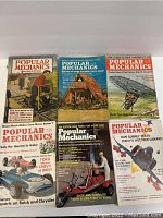 Six different vintage Popular Mechanics magazines displayed flat, covers visible with various automotive and mechanical themes